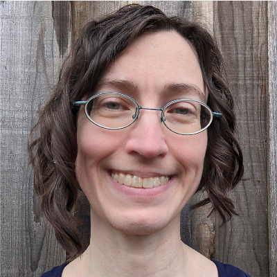 Headshot of a white woman with brown hair and blue metal glasses. She is smiling.